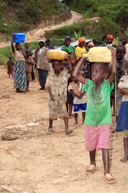 A group of African refugees carrying goods walk in line along a dirt road.